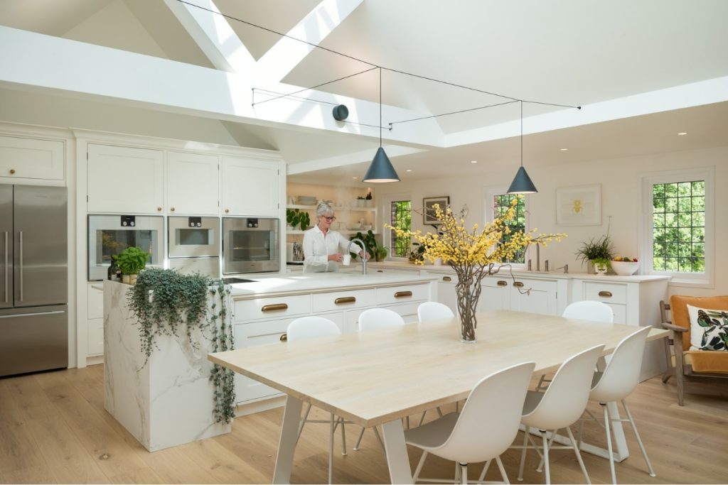 A light, open kitchen with a woman using a sink at the kitchen island